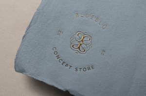 Logotipo circular de Blueblú en foil dorado sobre papel azul artesanal, detalle de branding premium.