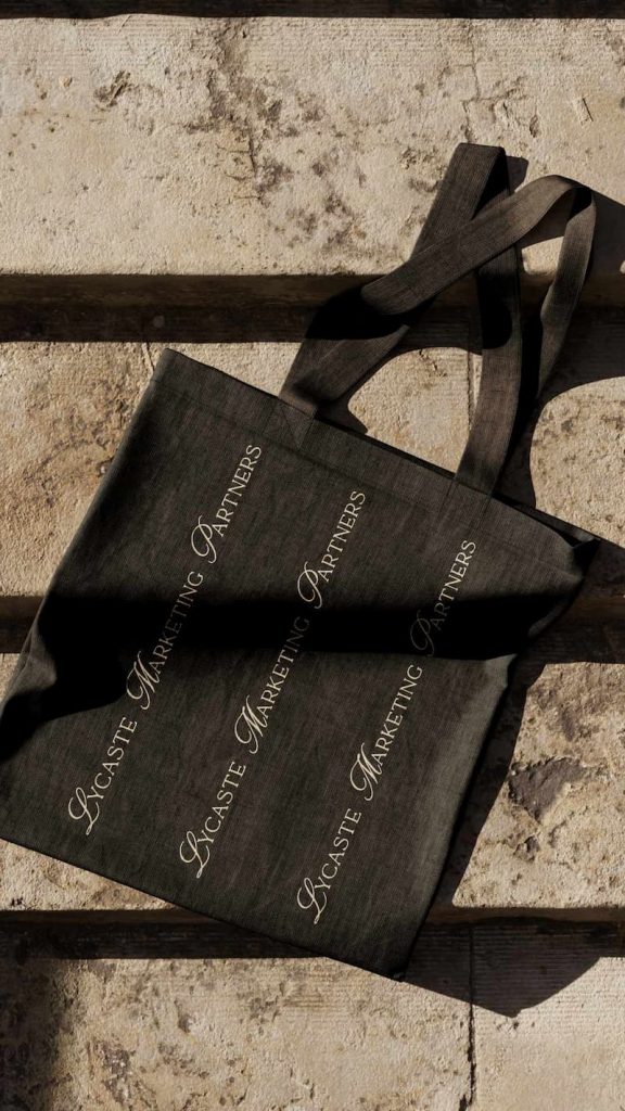Tote bag negra con repetición del logotipo de Lycaste Marketing Partners en estilo elegante.